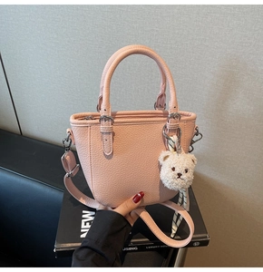 Close-up of pink litchi grain bucket bag with plush bear charm and striped silk scarf