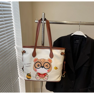 Detailed view of white tote bag with cute bear embroidery and brown shoulder strap on rack