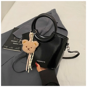 Detail of black glossy bucket bag with round handle and cute teddy bear charm accessory