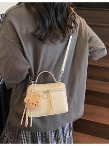 Chic cream bucket bag with top handle, crossbody strap and plush bear pendant detail