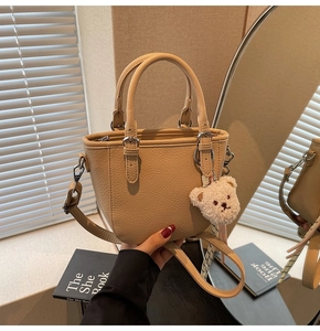 Detailed view of beige pebble leather handbag with plush bear charm and detachable strap