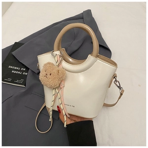 Detail of cream bucket bag with khaki handle, featuring a plush bear and woven charm