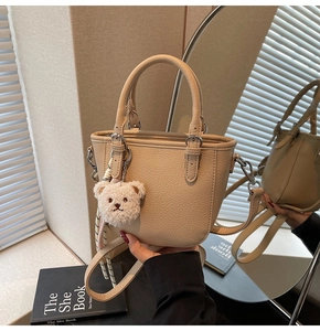 Detail of light khaki pebble grain tote bag with plush bear charm and silver hardware