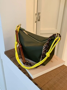 Dark green hobo shoulder bag with colorful woven straps on a pink book display