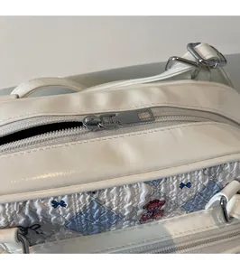 Detail of white leather shoulder bag featuring blue checkered bear print and silver zipper