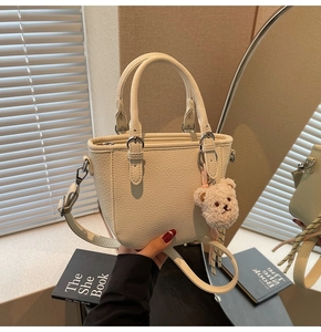 Detail view of a cream lychee grain mini tote bag with a cute plush bear charm decoration