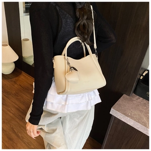 Detail view of cream bucket bag with lychee texture and heart charm shown on model