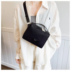 Détail du sac bandoulière en nylon noir avec écusson logo et large sangle sur chemise