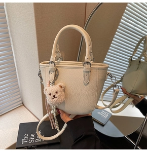 Detail of off-white lychee grain leather bucket bag with plush bear charm and silver hardware