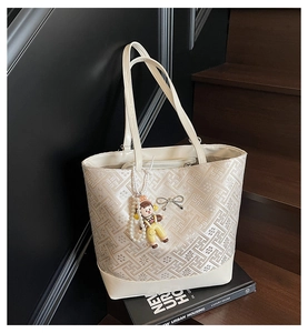 Detail of cream tote bag with geometric jacquard pattern and silver bow charm