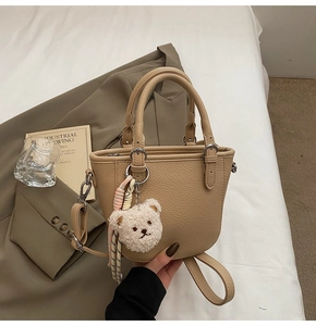Detail of beige bucket bag with plush bear charm and woven accessory on textured leather