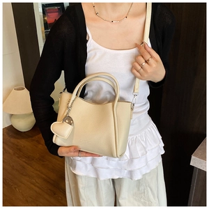 Beige litchi grain leather bucket bag with heart pendant and adjustable shoulder strap