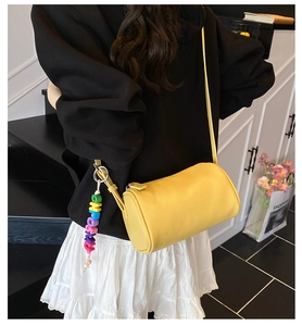 Detail of yellow pebbled leather cylinder bag with colorful beaded charm on a shoulder strap