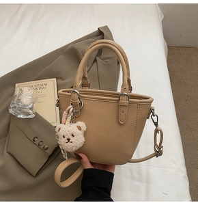 Detail of beige lychee grain leather handbag with cute plush bear charm and long strap