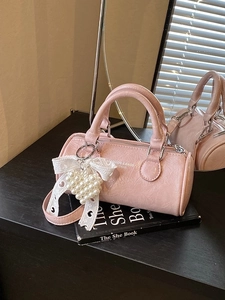 Pink cylinder handbag with textured faux leather and a pearl heart charm on books