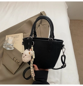 Detail of black lychee-textured bucket bag with cute bear charm on white fabric