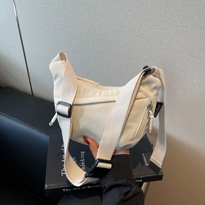 Detail of adjustable strap and plastic buckle on off-white nylon crossbody bag