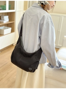 Detail of black crescent moon bag featuring a white heart motif and wide shoulder strap