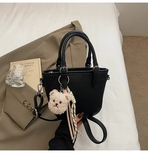 Detail of black pebbled leather bucket bag featuring a plush bear charm and woven cord decor