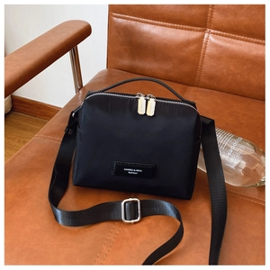Détail d'un sac bandoulière noir en nylon avec double fermeture posé sur un fauteuil en cuir