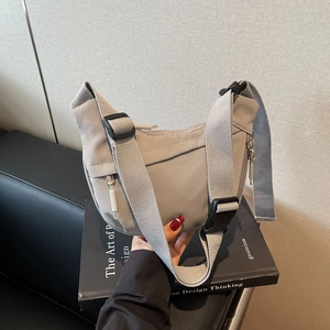 Close-up of light grey crescent crossbody bag with adjustable wide strap and zipper detail