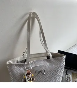 Detail of quilted tote bag with metal bow accent, pearl charm, and adjustable shoulder strap