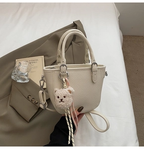 Creamy white bucket bag with pebble leather texture and a cute teddy bear charm