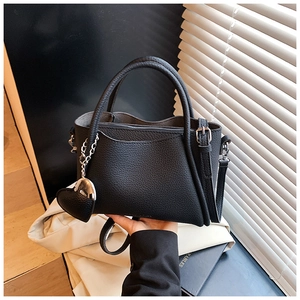 Detail of black pebbled leather tote featuring heart charm and adjustable shoulder strap