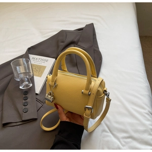 Detail of yellow lychee textured leather mini Boston bag with silver hardware on white linen