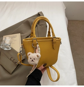 Detail of yellow pebbled leather bucket bag with cute teddy bear charm and strap