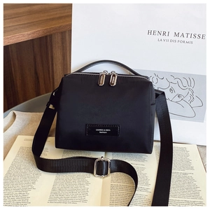 Détail du sac bandoulière en nylon noir avec sangle réglable sur fond de livre d'art