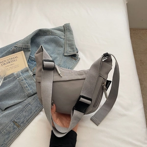Detail of gray nylon crossbody bag with adjustable strap and buckle on white bedding