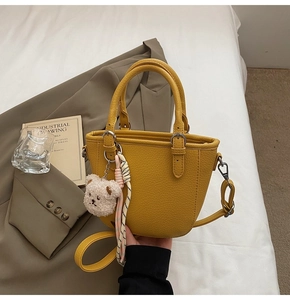 Detail of ginger leather bucket bag with plush bear charm on a warm lifestyle background