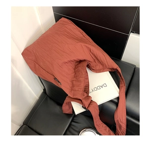 Dettaglio della borsa tote rosso ruggine con pieghe trapuntate su divano in pelle