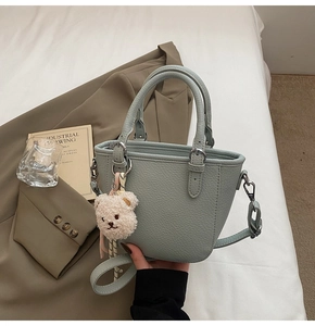 Detail of mint green bucket bag featuring pebbled leather texture and bear charm