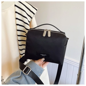 Détail du sac bandoulière en nylon noir avec double zip et poignée supérieure tissée