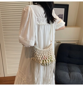 Detail view of white woven shoulder bag featuring bohemian fringe and wooden bead accents
