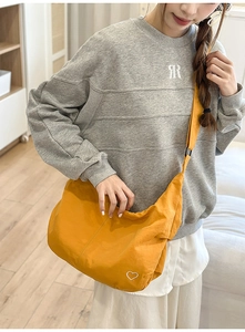 Model wearing a mustard yellow crossbody dumpling bag with white heart embroidery