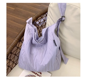 Dettaglio borsa tote plissettata lavanda con tracolla larga su sedia in vimini