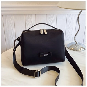 Gros plan sur un sac bandoulière en nylon noir avec double zip et plaque logo en métal