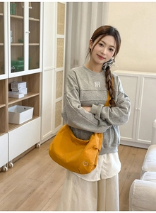 Detail of yellow canvas hobo bag with heart embroidery worn with casual sweatshirt
