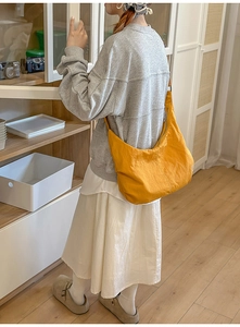 Detail of the bright yellow nylon half-moon crossbody bag shown on a model