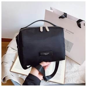 Détail du sac bandoulière en nylon noir avec plaque métallique et double fermeture