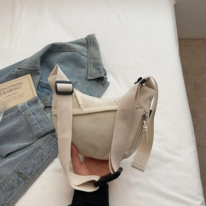 Detail of off-white crescent crossbody bag with adjustable wide strap on white surface