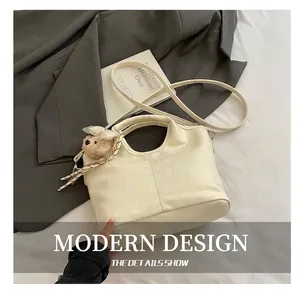 Detail of cream crocodile texture handbag with cute bear charm and shoulder strap