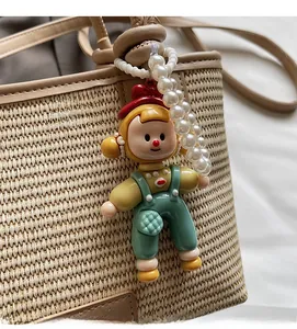 Detail of cartoon doll charm with faux pearl chain on a beige woven bucket bag