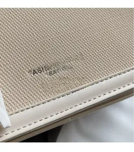 Close-up of woven fabric and leather texture on a beige fashion handbag with logo