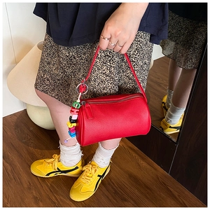 Close-up of a red leather cylinder Boston bag with colorful beaded charm on a model