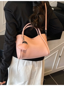 Pink lychee grain leather handbag with heart charm shown from a side-view on a model