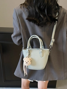 Mint green pebble leather bucket bag with bear charm worn by a model in casual blazer